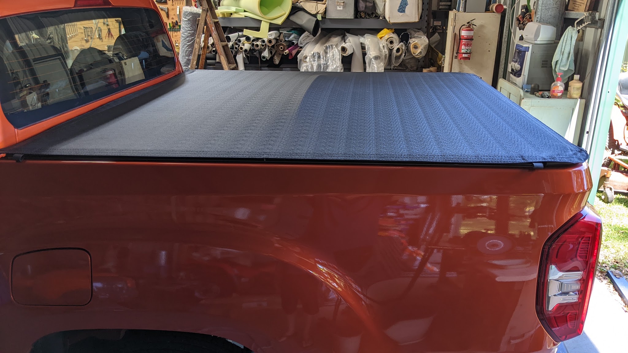 A soft tonneau cover fitted to the tray of an orange ute inside the workshop