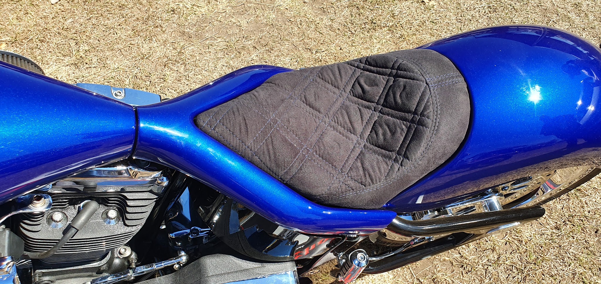 A diamond stitched suede seat on a metallic blue cruiser motorcycle