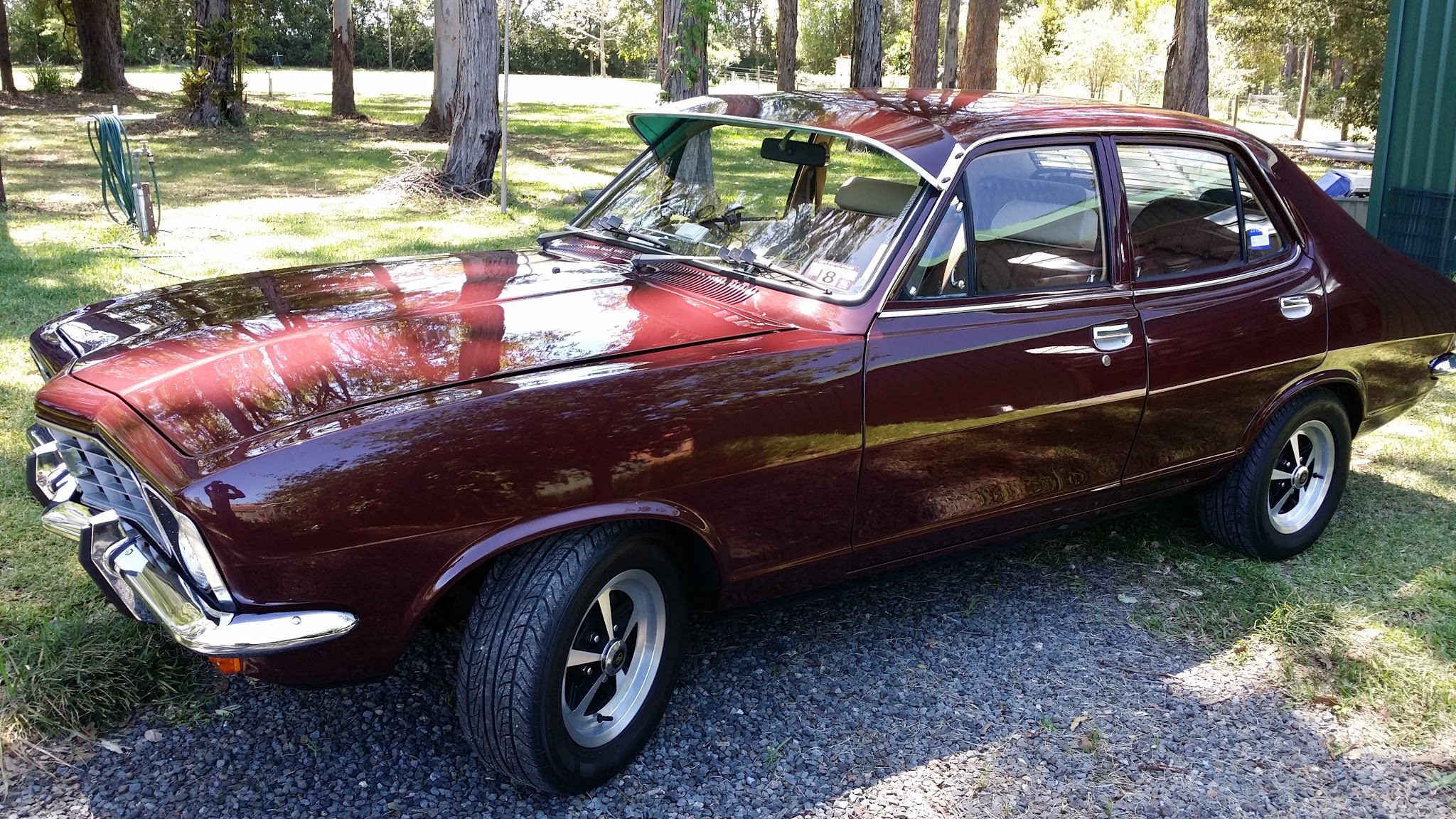 A finished maroon nineteen seventies Holden sedan parked on gravel at a rural property
